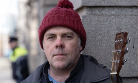 Martin Leahy wearing a red bobble hat holding a guitar.