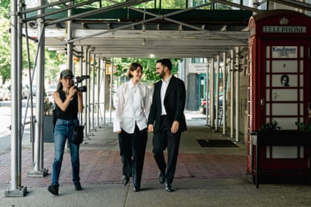 a man and a woman hold hands as a person holding a camera walks beside them