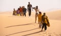 A line of people walking across sand dunes
