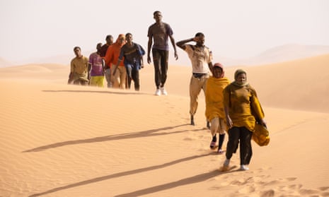 A line of people walking across sand dunes in the Sahara desert