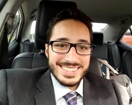 Man in suit and glasses smiling in selfie taken in car.