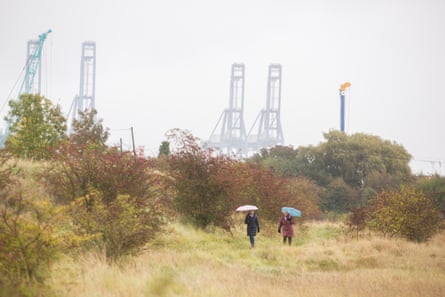 Two people with raised umbrellas walking through scrubland
