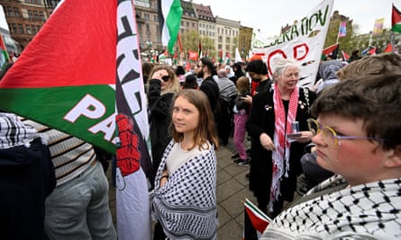 Greta Thunberg stands with with other people wearing keffiyehs and carrying banners and protest signs