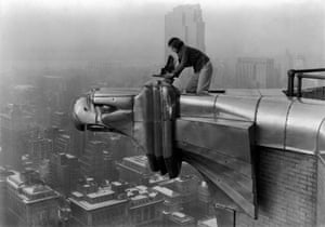 American photographer and journalist Margaret Bourke-White perches on an eagle head gargoyle at the top of the Chrysler building and focuses a camera, New York, 1935