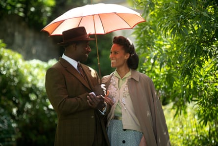 Two actors share an umbrella, smiling at each other