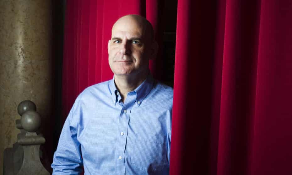 Harlan Coben in a pale blue shirt, standing next to red curtains