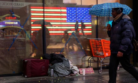 A person using an umbrella walks past a homeless person in New York City.