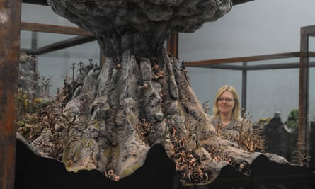 A woman with glasses smiles while looking at Fucking Hell by Jake and Dinos Chapman, a fibreglass artwork with miniature soldiers, skeletons and figures under a mushroom cloud