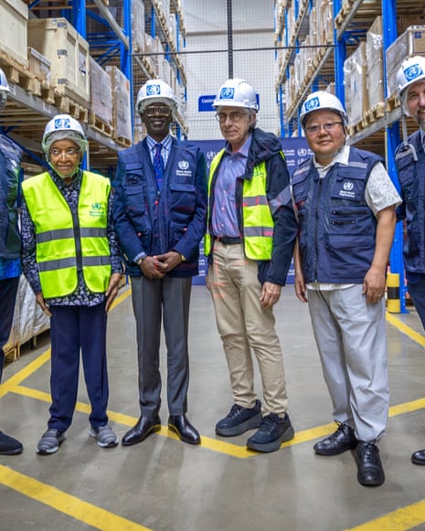Six people including Denis Mukwege and Ellen Sirleaf in hard hats stand in a warehouse with blue racking