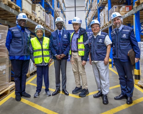 Six people including Denis Mukwege and Ellen Sirleaf in hard hats stand in a warehouse with blue racking