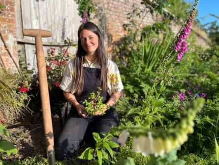 Frances Tophill kneeling in a cottage-style garden holding a small plant