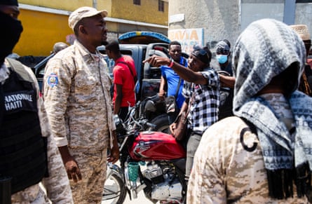 a man argues with a police officer as people stand outside