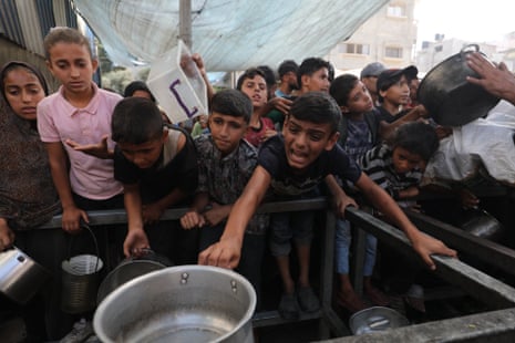 Palestinians wait in long lines to receive hot meals distributed by a charity organization at the Nuseirat area.