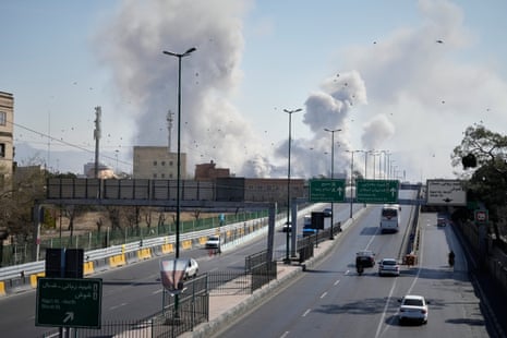 View of a major road as smoke rises in the air in the background.