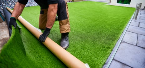 A tradie rolls out fake bright green synthetic grass in a backyard