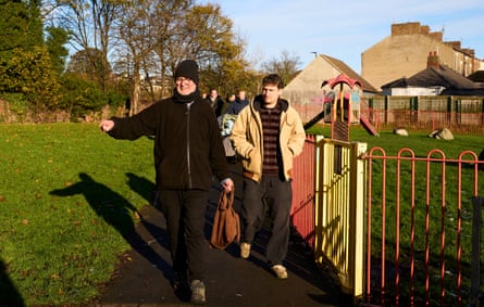 People follow Hughes as they pass the red and yellow railings of a playground in a park