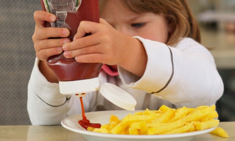 A toddler squeezes tomato ketchup on to a plate of chips.