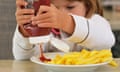 Young girl squeezing tomato sauce on to a plate of chips