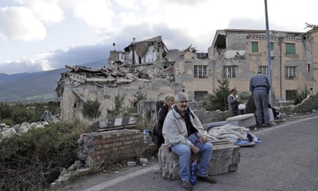 People sit on the side of a road in front of collapsed buildings following the earthquake in Amatrice, Italy