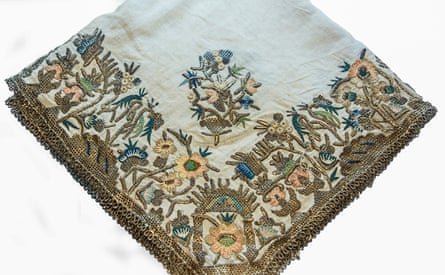A handkerchief with an border of elaborate floral embroidery in golds, ellows and blues.