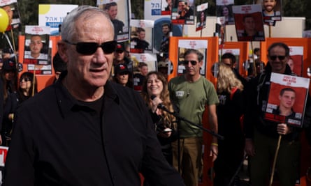 Benny Gantz seen here with families and supporters of the hostages on a march calling for their release – he is wearing black sunglasses and a black sweater and is standing in front of a crowd of people holding placards with pictures and names of those missing