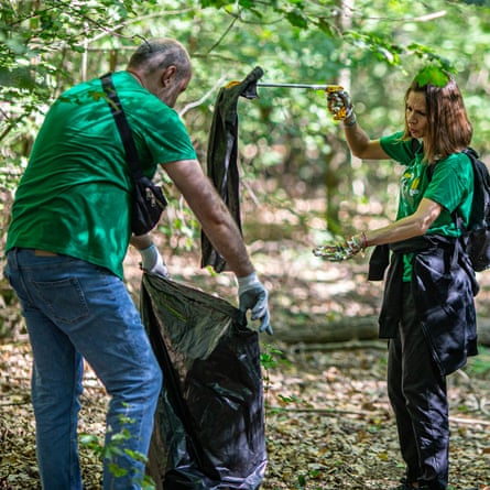 دو نفر با تیشرتهای سبز در حال جمعآوری زباله در یک کیسه زباله