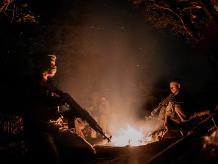 Rangers holding AK-47 assault rifles sit next to a campfire at night