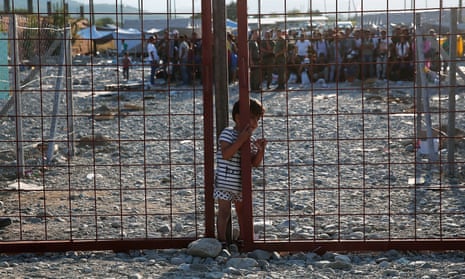 A young boy slips through a narrow opening in a gate inside a refugee camp in Macedonia.