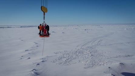 Four people are suspended on what appears to be a crane over an icy landscape