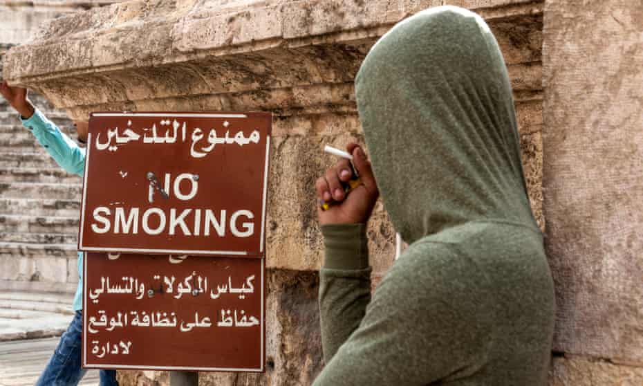 A man smoking in front of no smoking sign in Amman, Jordan. 
