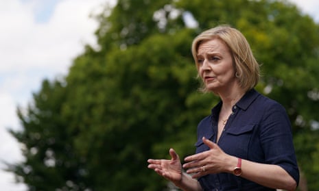 Liz Truss outdoors, speaking at a campaign event, gesturing with both hands against a backdrop of trees