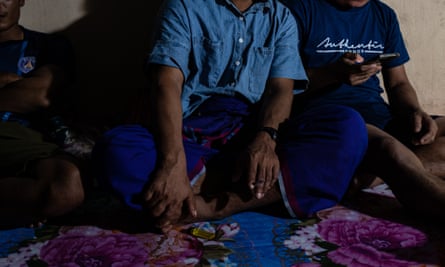 Three men sitting on a cloth while one looks at a phone