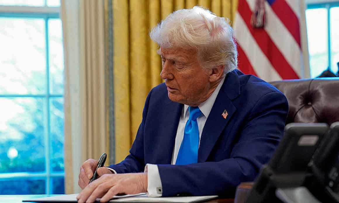 The US president signs a piece of paper in his office