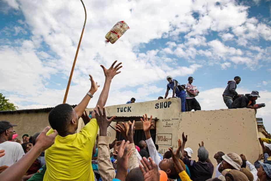 Crowd of people raise their hands trying to catch food thrown from a small shop