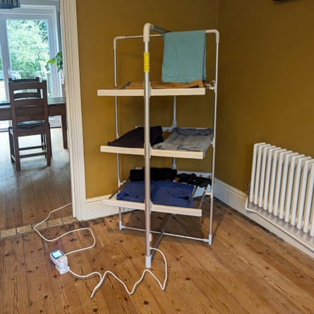 A heated three-tier clothes airer with folded laundry stands plugged into an electrical timer