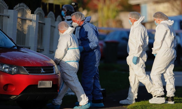 Police investigators wearing protective suits walk into a home past a red car