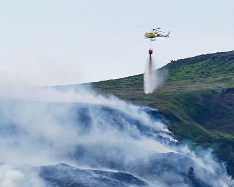 A helicopter dropping a payload of water on to a burning hillside