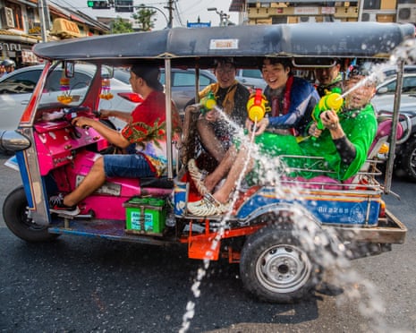 People in a tuk tuk spray water guns while riding through a street during a water fight