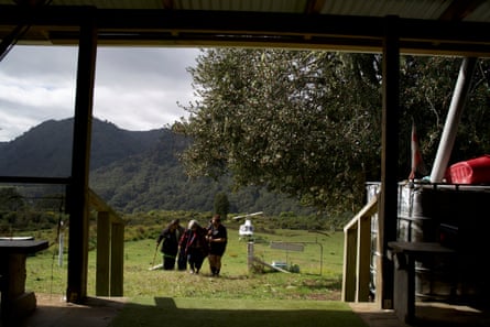 View from inside a house with three people walking up a hill.There is a helicopter in the paddock in the background
