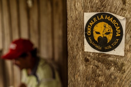 An anti-mining sticker on a wooden post. A man sits in the background, out of focus.
