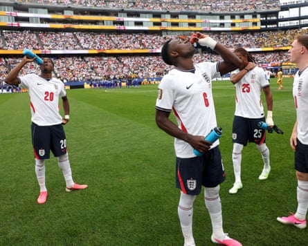 Marc Guehi takes a drink and holds a blue bottle, while Noni Madueke also swigs from a bottle behind him. Other players stand around holding drinks bottles.