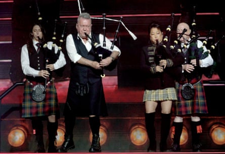 Jimmy and Jane Barnes on stage surrounded by other bagpipe players