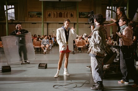 Styles in off-white, oversize blazer and red shorts surrounded by video production crew