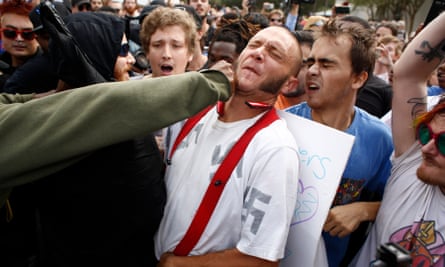 A man wearing a shirt with swastikas on it is punched by an unidentified member of the crowd near the site of a planned speech by Richard Spencer.