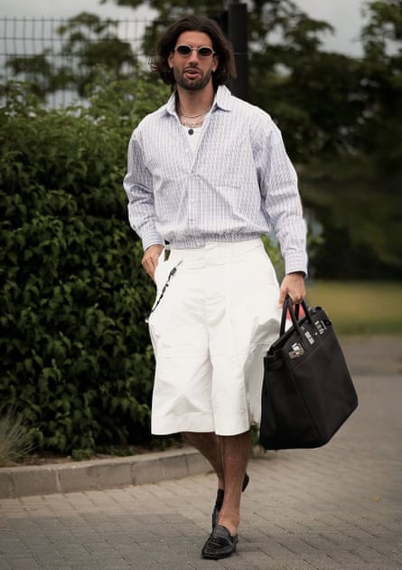 Dominik Szoboszlai in long-sleeved shirt and white culottes, clutching a black travel bag