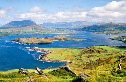 A view of the edge of a green island dipping into a blue sea, taken from up high, with more islands and mountains in the distance.