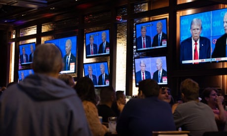 people look at a wall of eight screens showing two white men in suits