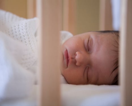 A baby lies sleeping in her cot