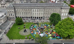 A cluster of tents on the grass in a courtyard surrounded by old buildings.