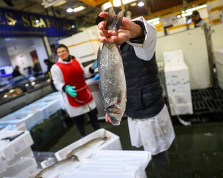 A fishmonger picks up a sea bass at Billingsgate fish market